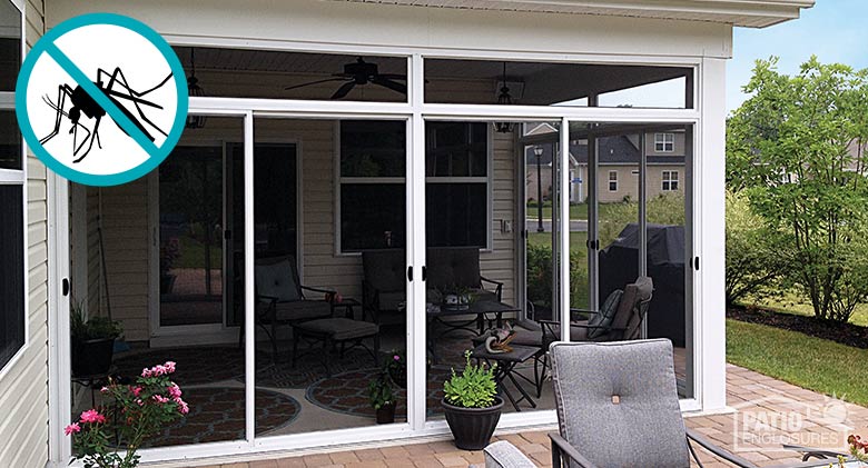 The exterior of a corner patio enclosed with a screen room with a white frame, bushes on the right.