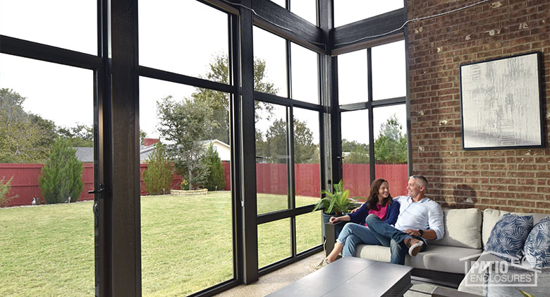 A couple relaxing together as they take in their backyard view from inside their sleek black patio enclosure.