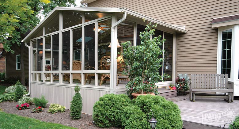 A tan gable-roofed sunroom with glass wings and glass knee wall.
