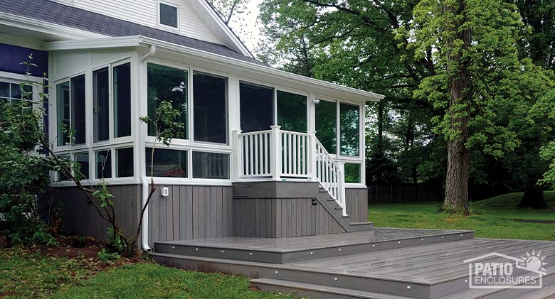 A white glass sunroom with glass knee wall and single-sloped roof. Stairs lead down to deck area.