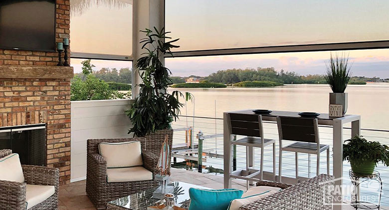 The interior of a covered patio on the water with the openings covered in part by opaque retractable screens