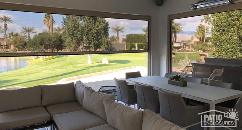 A dining table and chairs along with a large sofa inside a covered patio with retractable screens on the openings.