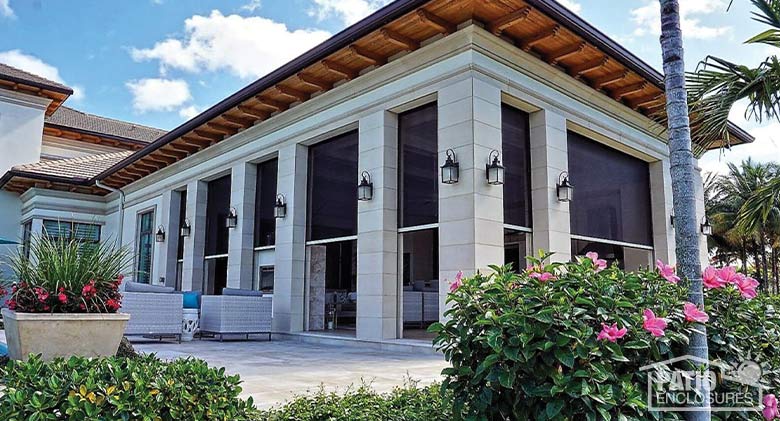 A large, covered patio with white stone columns and black motorized retractable screens partly covering the openings.