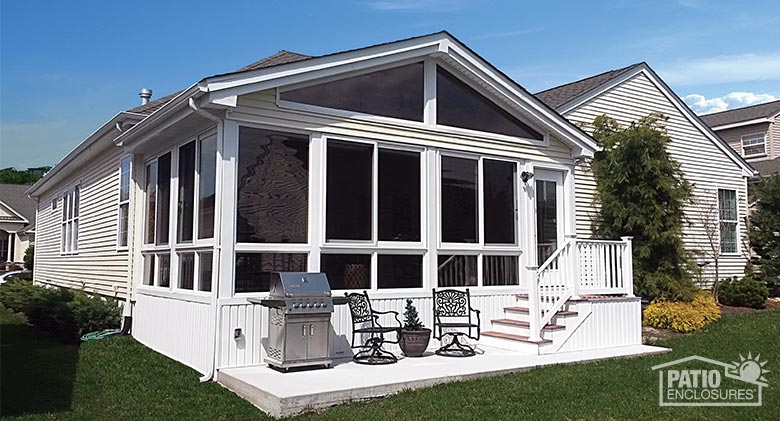 A large white sunroom with gable roof, glass knee wall, and glass wings. Stairs lead down to a small patio with grill.