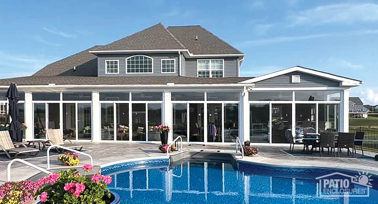 A pool and large patio in front of a glass patio enclosure spanning the entire width of the home.