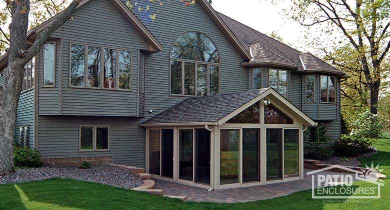 Sandstone all season sunroom with vinyl frame and shingled, gable roof.