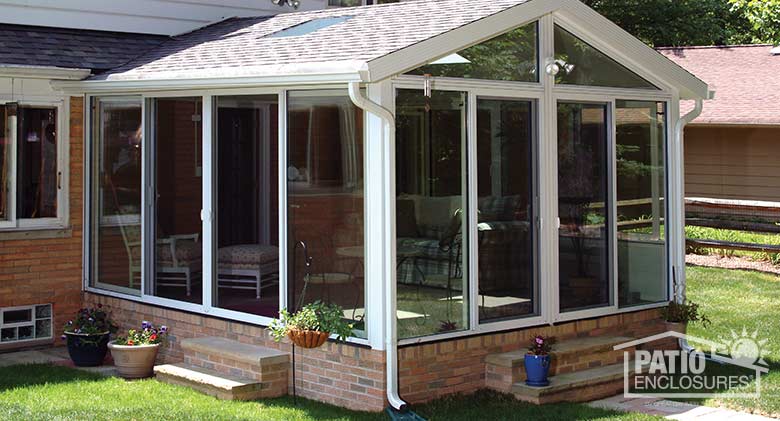 White four season sunroom with aluminum frame and shingled gable roof with glass roof panels.