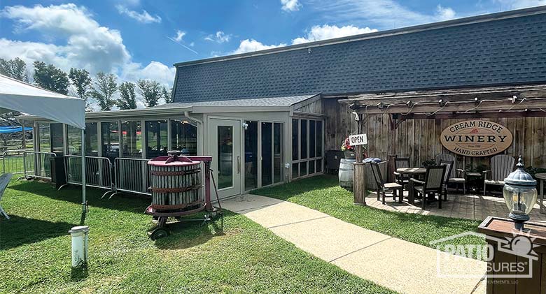 Exterior photo of a winery with a beige sunroom on the left and outdoor tables and chairs on the right