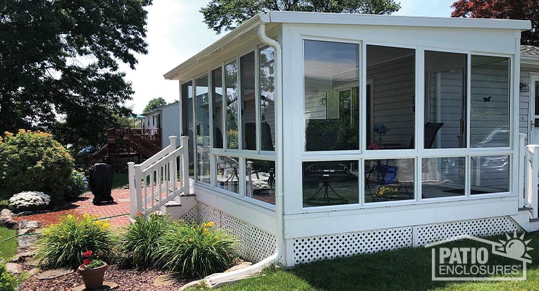 white three-season sunroom with single-sloped roof and glass knee walls, patio with grill in background