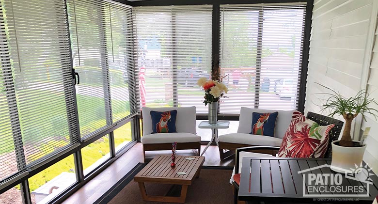 interior of a sunroom with partially open mini-blinds, two chairs and table in the background and a table in the foreground