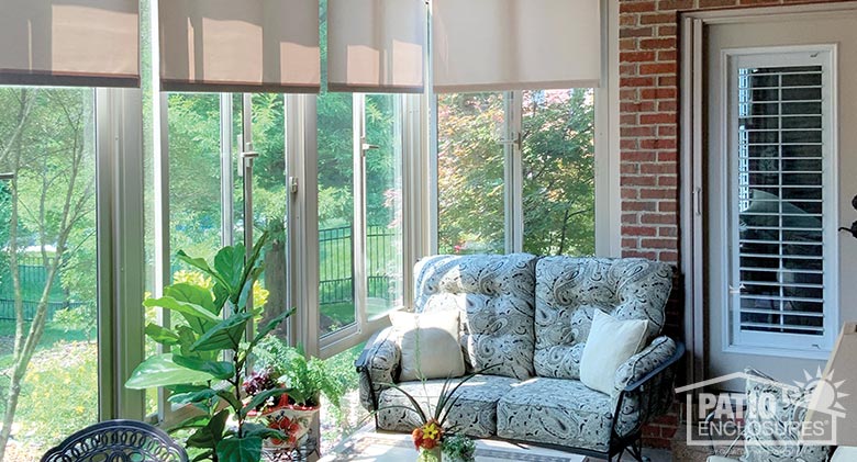 sunroom interior featuring loveseat with pillows, plant in foreground and sun streaming in