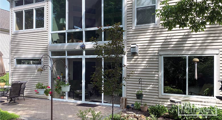 two glass-enclosed back porches, one above the other, with patio, landscaping and bird feeders in foreground