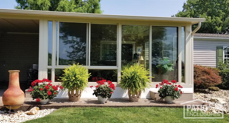 beige glass sunroom exterior with potted plants and flowers in front