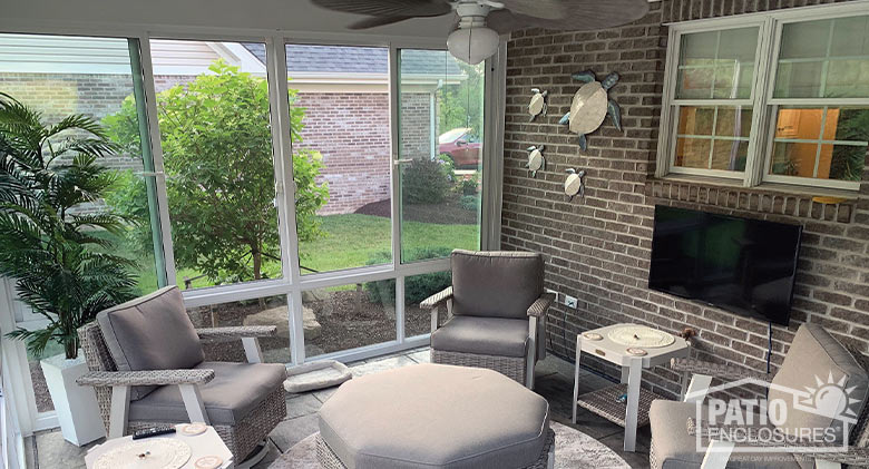 interior of porch enclosure, brick wall with mounted TV, comfortable seating area, ceiling fan, turtle décor on wall