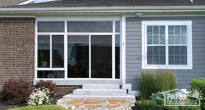 nicely landscaped exterior with three steps leading to all-glass porch enclosure on back of gray house