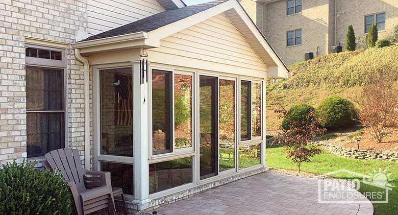 Four season room in sandstone with vinyl frame and glass knee wall enclosing an existing covered patio.
