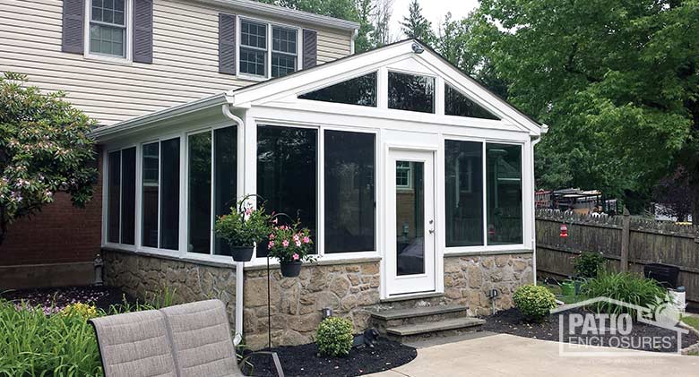 Three season room in white with insulated glass and stone knee wall enclosing an existing screen room.