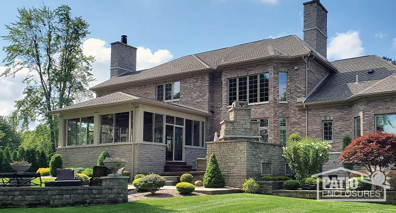 Exterior view of a sandstone enclosed porch with hip roof and stone knee wall on a large brick home.