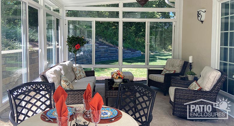 Interior of a white sunroom with set dining table in the foreground and a comfortable seating area behind it.