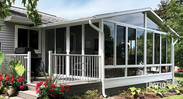 Exterior of a white sunroom with gable roof, glass knee walls and a deck off the patio doors to the left.
