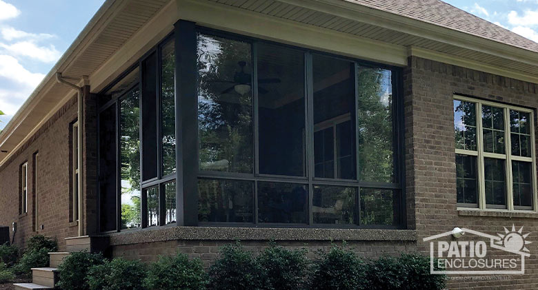 Four steps lead up to a corner patio enclosed with glass in a bronze frame, attached to a brick home.