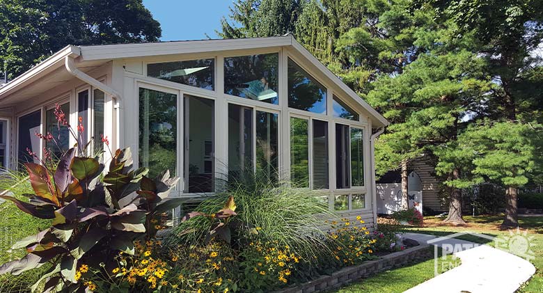 Lovely landscaping of Black-eyed Susans and ornamental grasses line a walkway leading to a large sunroom with gabled roof.