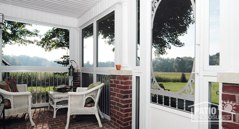 Wicker furniture on a screened-in, brick front porch with picket railing, a wooden screened door and bead-board ceiling.