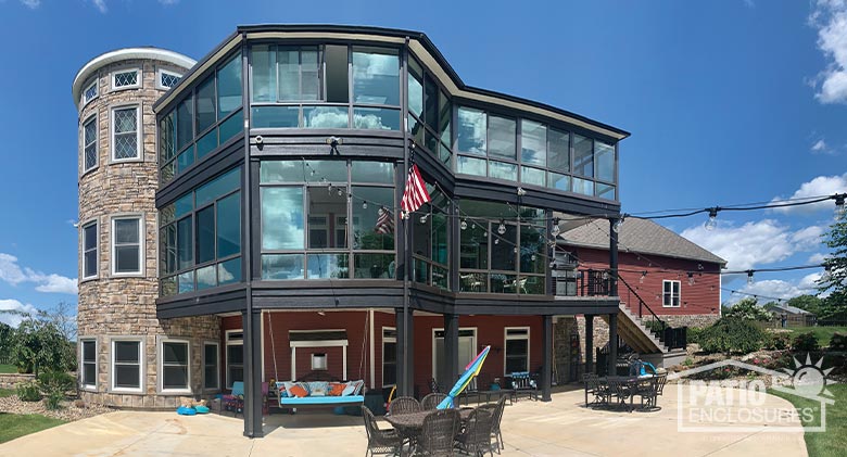 Two stories of glassed-in decks over a covered patio with porch swing attached to a three-story red home with stone turret.