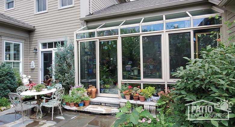 A bump-out solarium enclosed a porch surrounded by plants and a patio with dining table and four chairs.