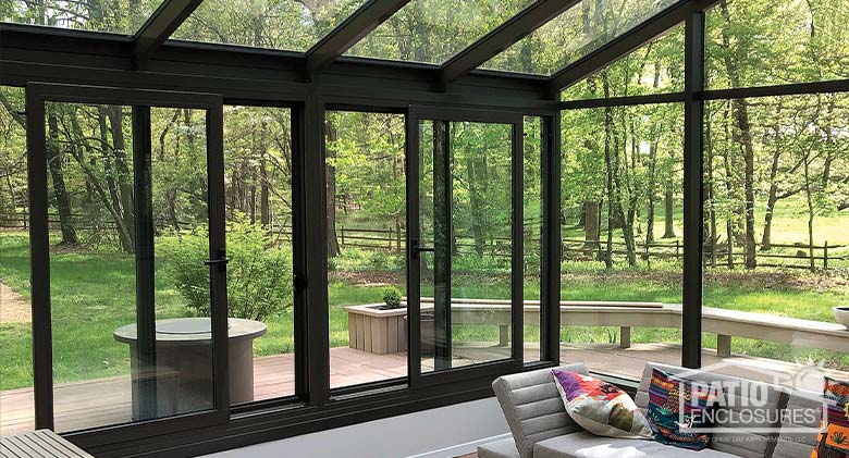 Interior of a solarium with glass roof and view of park-like setting. A modern couch and bright pillows in the foreground.