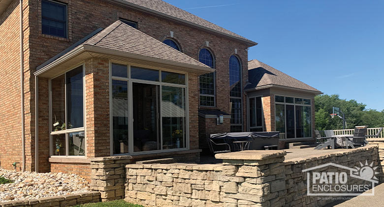 A modern brick home with two enclosed covered patios on either side of the back. A stone wall and patio in the foreground.