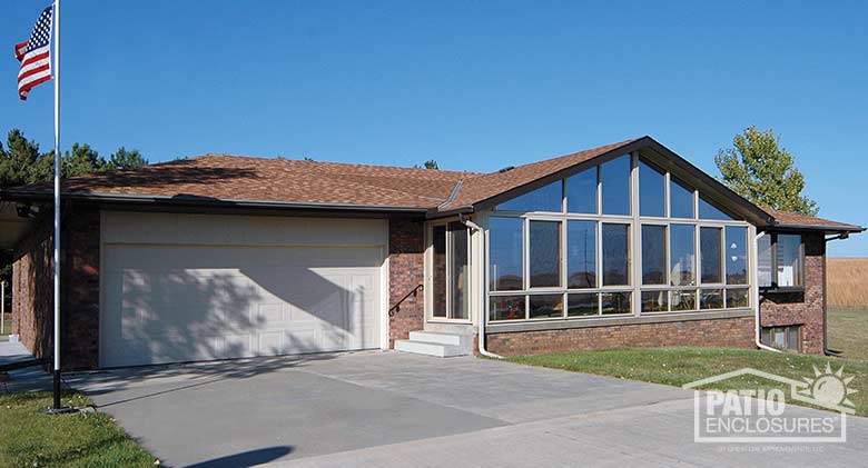 Sandstone four season sunroom with aluminum frame, glass knee wall and shingled gable roof.