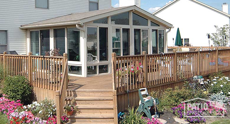 Sandstone four season sunroom with vinyl frame, glass knee walls and shingled, gable roof.