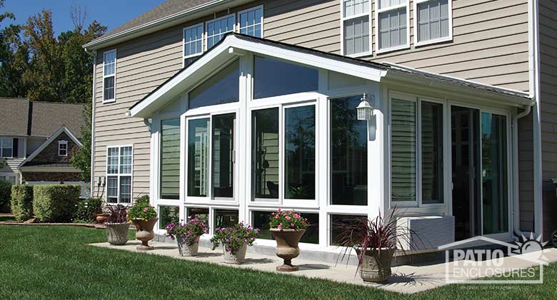 White four season sunroom with vinyl frame, glass knee walls and shingled, gable roof.