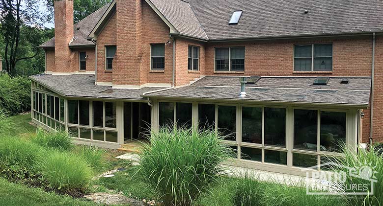 Two sandstone four season rooms with vinyl frames, glass knee walls and shingled, single-sloped roofs.