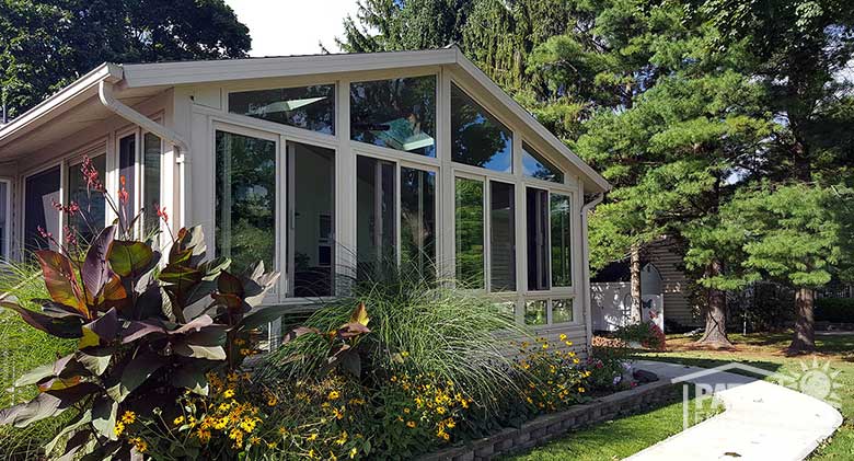 Sandstone four season sunroom with vinyl frame, glass knee walls and shingled gable roof.