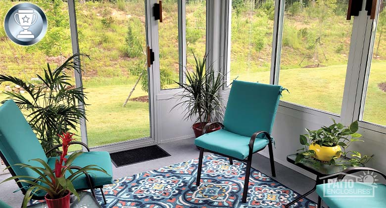Bright teal cushions on black metal chairs, plants and a brightly patterned rug are the décor for a white sunroom.