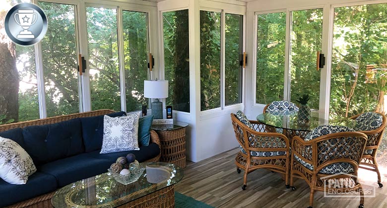 Sunroom interior with wood floor, wicker couch with blue cushions, coffee table and glass dining table with four chairs.