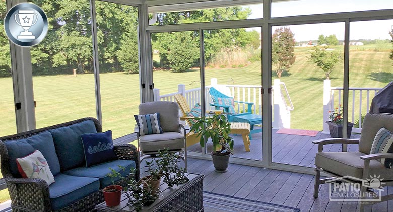 Screen room on a deck with wicker couch, two side chairs and coffee table. Two brightly colored Adirondack chairs outside.