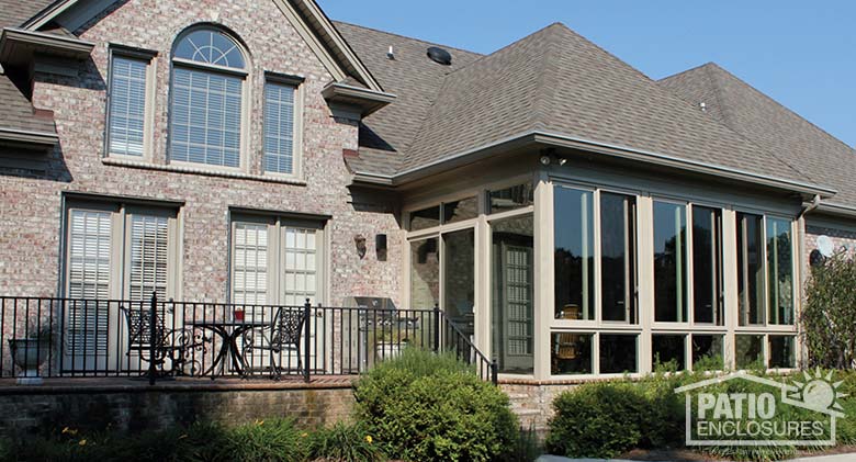 Sandstone three season sunroom with glass knee wall enclosing an existing covered porch.