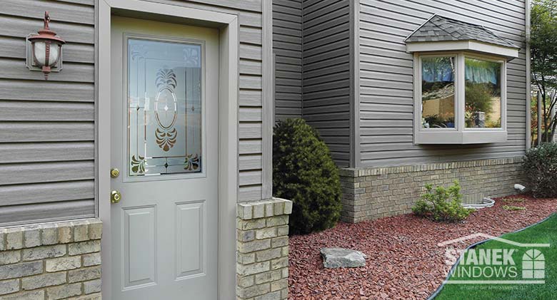 Legacy Steel Provia® entry door in gray with etched glass and three-lite bay window with shingled hip roof in background.
