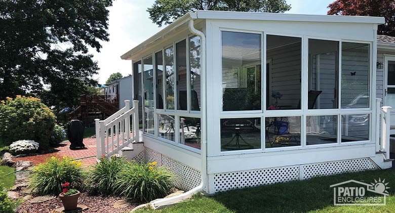 A glass patio enclosure with single-sloped roof, foam wings, and glass knee walls. Day lilies and potted plant in front.
.