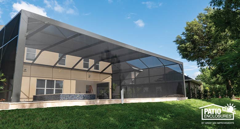 Trees and lawn surround a bronze pool enclosure with mansard roof and picture window screen on the front.