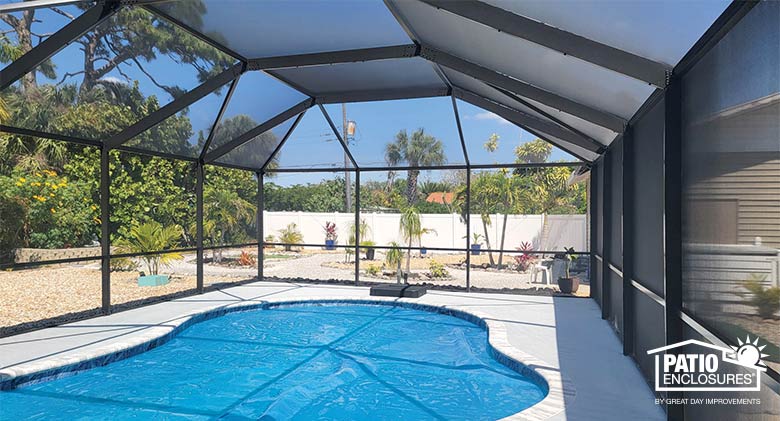 The interior of a bronze pool enclosure with mansard roof surrounding a kidney-shaped pool. A view of a neat yard outside.