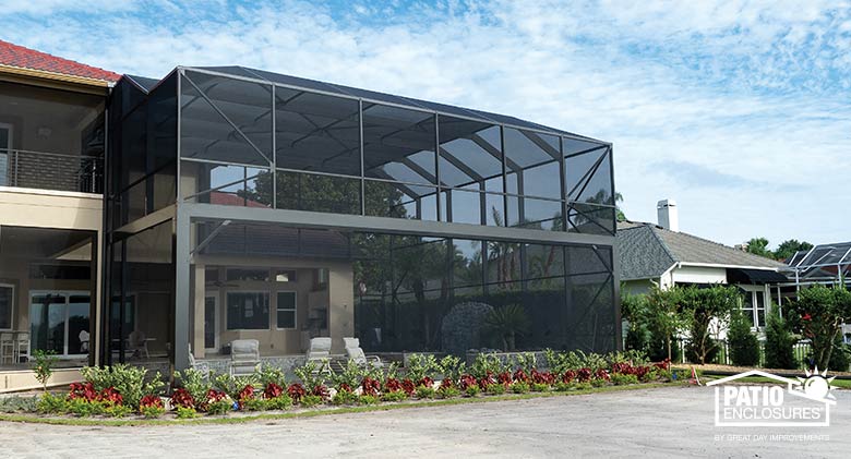 A two-story bronze pool enclosure with mansard roof, picture window screen on the bottom level, and neat plantings around.