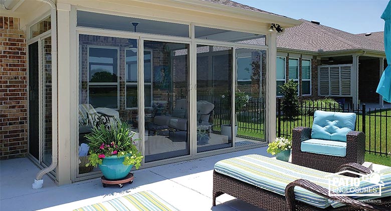 Exterior of a glass Florida room patio enclosure with tan frame. Lounging furniture and potted plants on the outdoor patio.