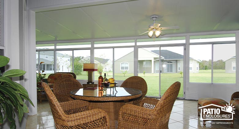 A large white Florida room enclosed with glass and furnished with a wicker table, chairs, and comfortable seating area.