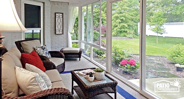Cushioned brown wicker furniture in a glass Florida room with views of the garden and yard.