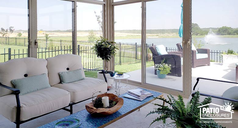 Plants thrive in this glass Florida room with beige cushioned furniture, blue pillows and a blue coffee table.