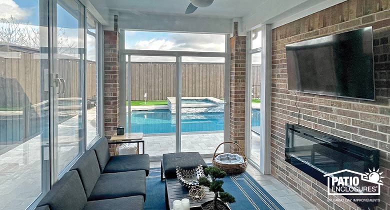 A cozy glass-enclosed patio with large TV and wall-mounted electric fireplace with views of the outdoor pool.